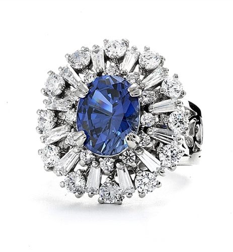 Diamond Essence Ring in Platinum Plated Sterling Silver with 2.5 carat Oval Sapphire Essence in the center, surrounded by Diamond Essence round stones and baguettes. Appx. 4.5 cts.t.w. on designer wide band. Just perfect for all occasions.